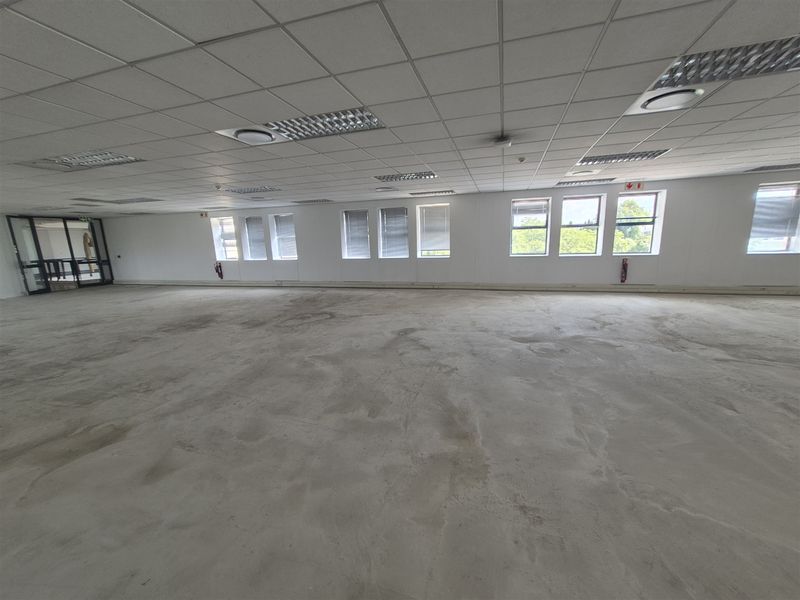 A large, open-plan office space featuring a suspended ceiling, recessed lighting, and expansive windows, currently awaiting flooring installation and final fit-out.