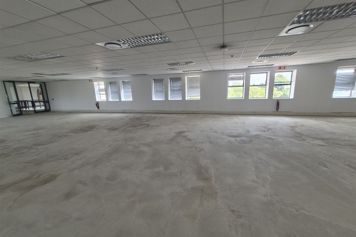 A large, open-plan office space featuring a suspended ceiling, recessed lighting, and expansive windows, currently awaiting flooring installation and final fit-out.