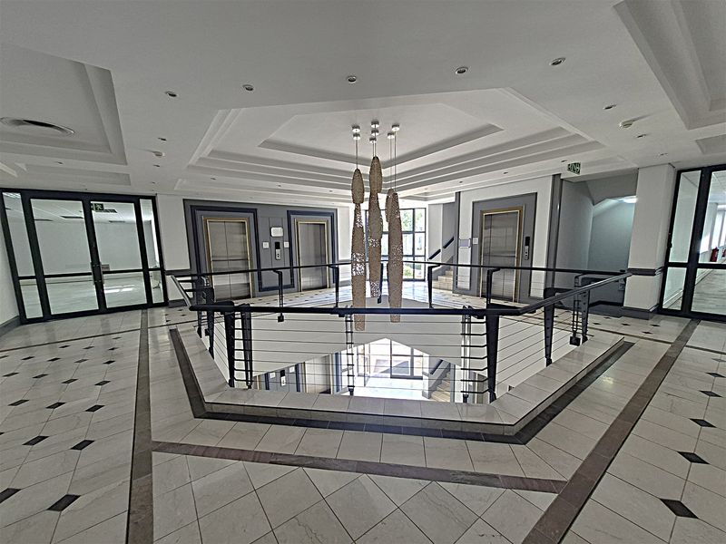 Spacious office building lobby featuring a central atrium, multiple elevators, elegant tiled flooring, and a decorative coffered ceiling with recessed lighting.