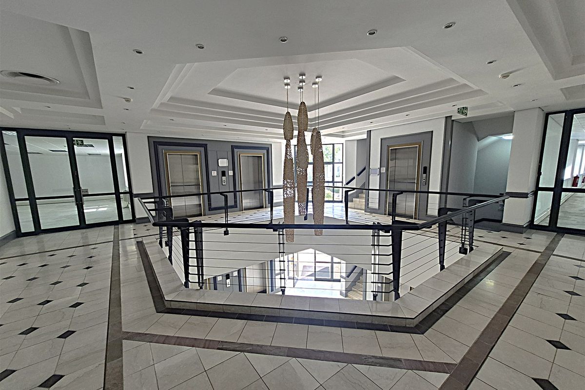 Spacious office building lobby featuring a central atrium, multiple elevators, elegant tiled flooring, and a decorative coffered ceiling with recessed lighting.