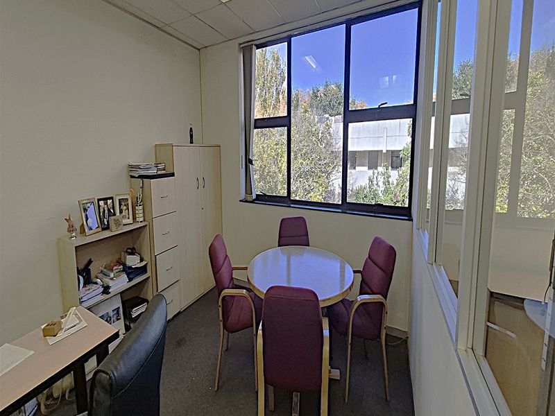 A functional office space featuring a large window, suspended ceiling, and glass partition wall, providing a bright and professional work environment.