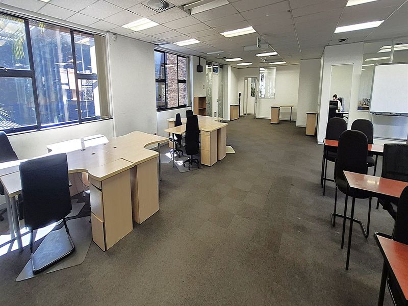 Spacious open-plan office area featuring suspended ceilings, recessed lighting, and large windows providing natural light, suitable for a professional workspace.