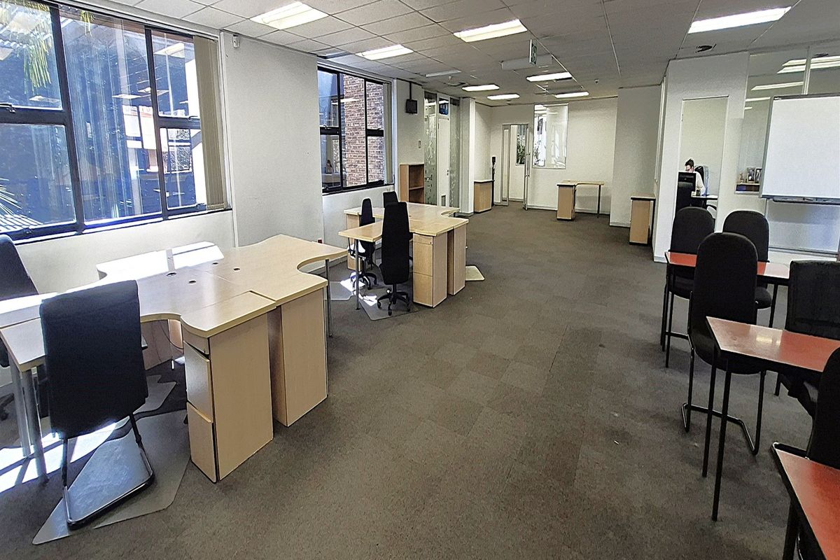 Spacious open-plan office area featuring suspended ceilings, recessed lighting, and large windows providing natural light, suitable for a professional workspace.