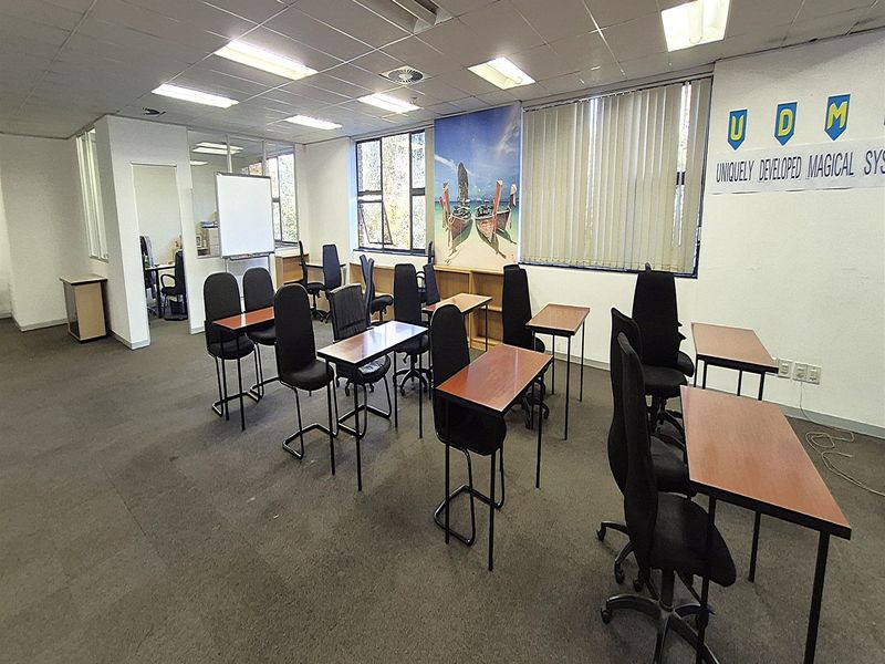 A functional office space featuring a suspended ceiling, recessed lighting, carpeted flooring, and glass partitions, suitable for a training or meeting room setup.