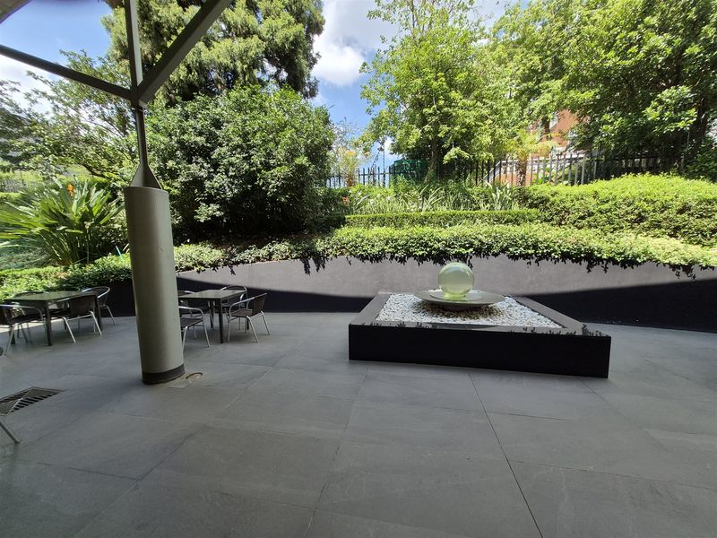 A well-maintained covered patio area featuring large format floor tiles, a modern water feature, and landscaped garden views.