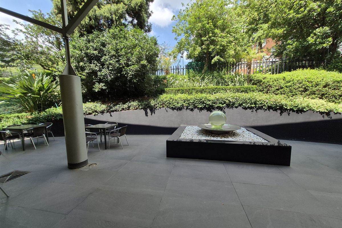 A well-maintained covered patio area featuring large format floor tiles, a modern water feature, and landscaped garden views.