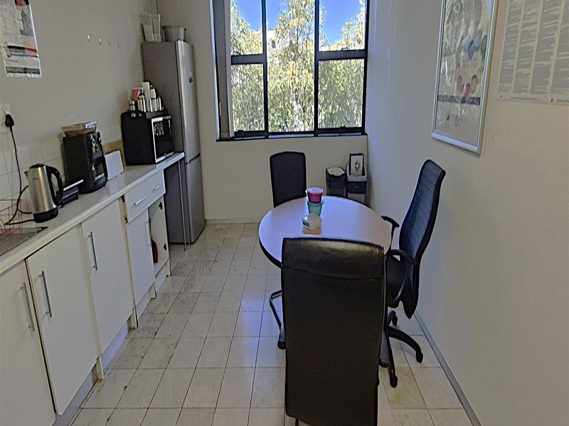A compact office kitchenette featuring built-in cabinetry, tiled flooring, and a large window providing natural light.