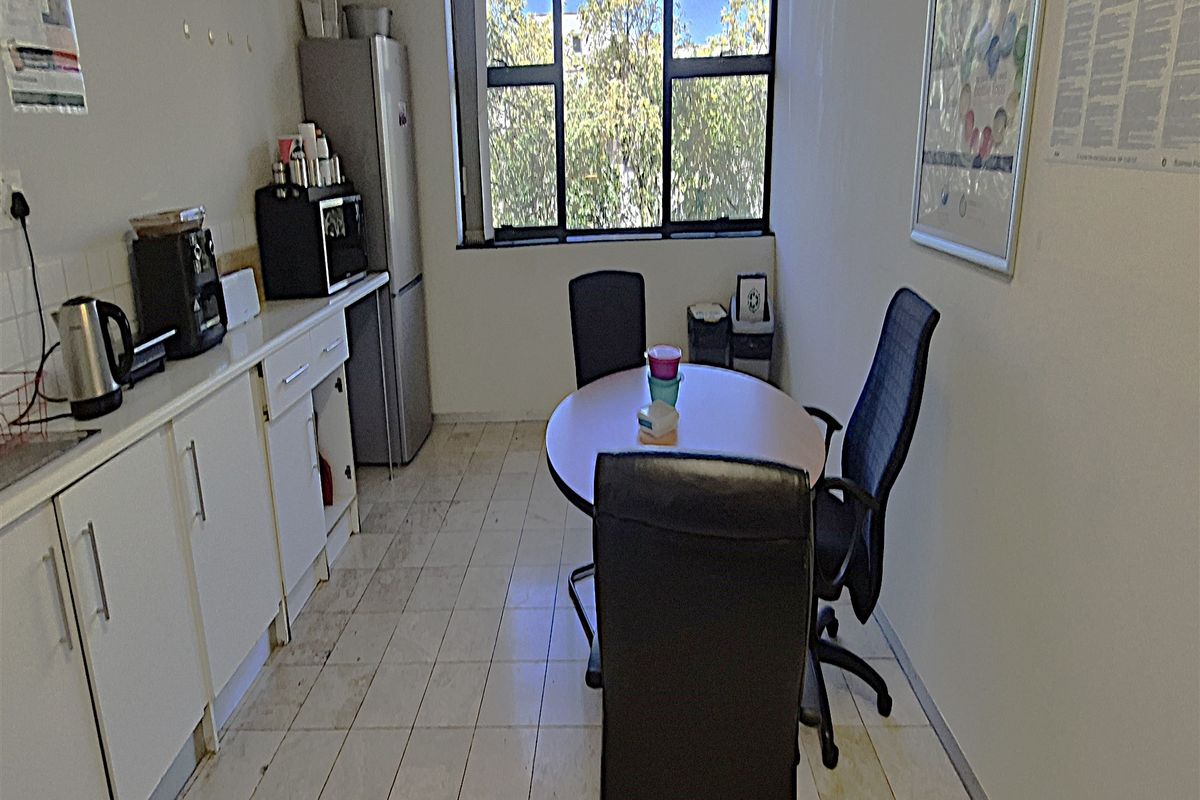 A compact office kitchenette featuring built-in cabinetry, tiled flooring, and a large window providing natural light.