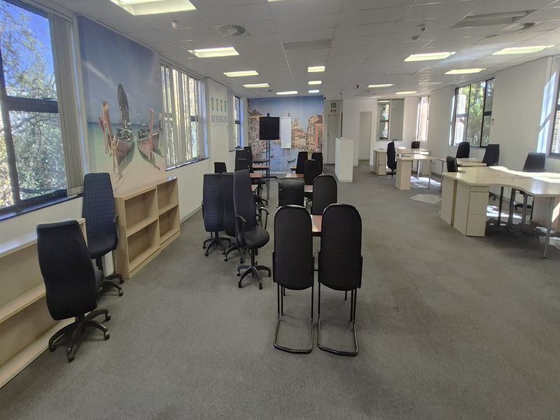Spacious open-plan office area featuring large windows, suspended ceilings with recessed lighting, and built-in shelving units.