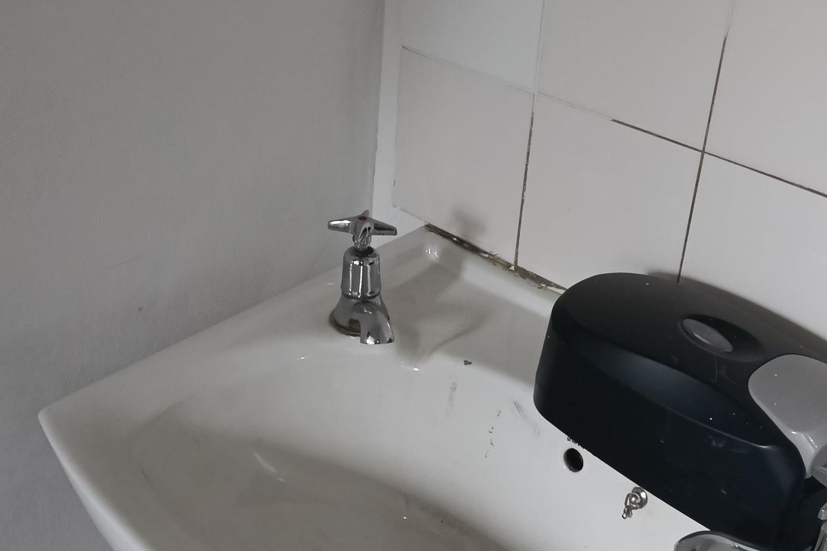 A functional industrial-style hand wash basin featuring a wall-mounted faucet and tiled splashback, suitable for utility or washroom areas.