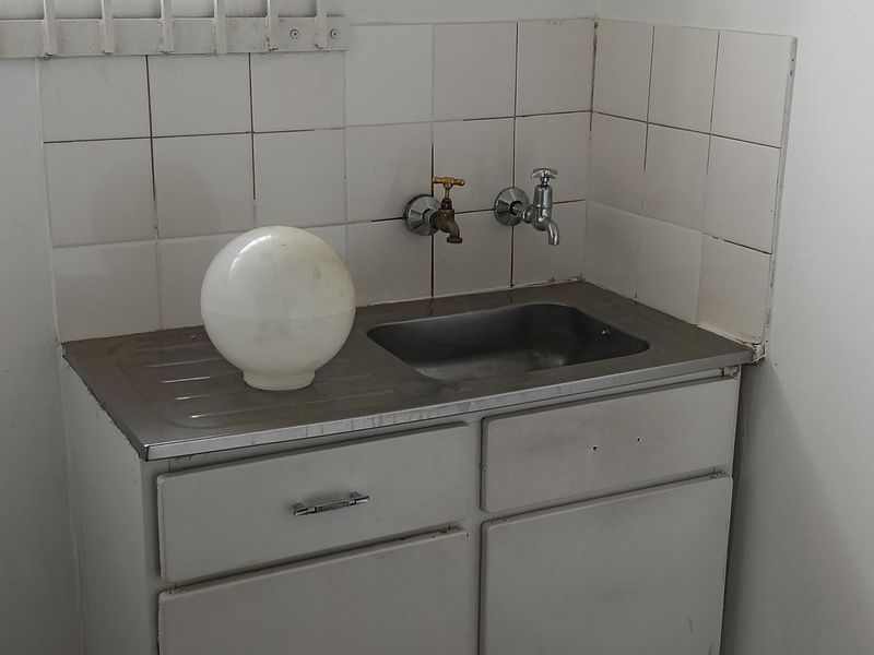 A functional utility area featuring a stainless steel sink, built-in cabinetry, and tiled splashback, situated beneath a window with security bars.