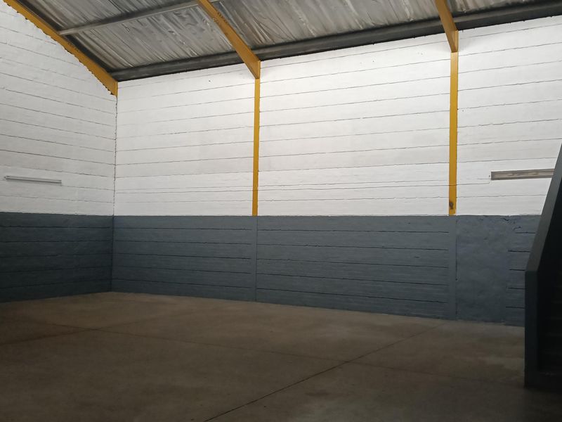 Spacious industrial warehouse unit featuring high ceilings, exposed steel support beams, painted masonry walls, and durable concrete flooring.