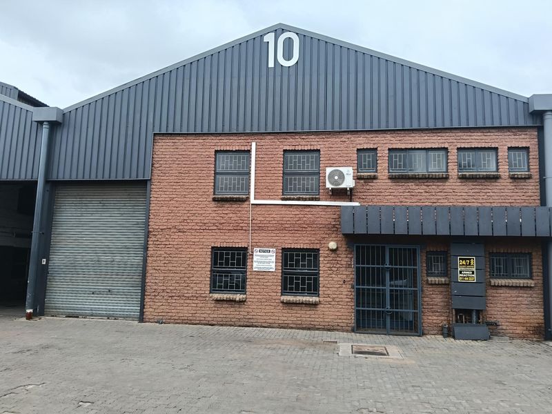 Industrial unit facade featuring exposed brickwork, a large roller shutter door, secure metal entrance gate, and high-level metal cladding.