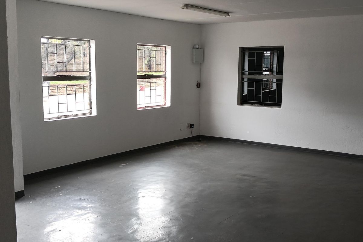 An empty industrial office space featuring painted concrete flooring, white walls, and security-barred windows providing natural light.