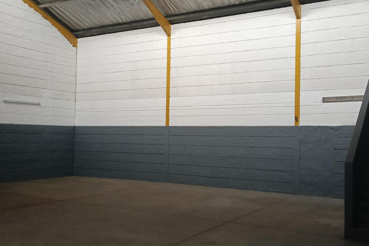 Spacious industrial warehouse unit featuring high ceilings, exposed steel support beams, painted masonry walls, and durable concrete flooring.