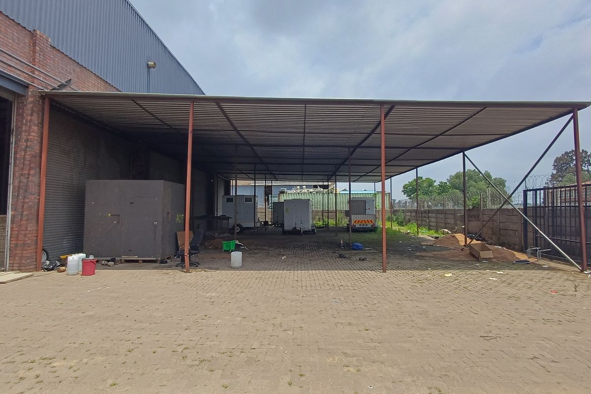 Large industrial covered outdoor storage or loading area with a metal roof structure, paved flooring, and perimeter fencing.