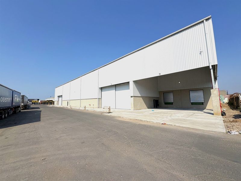 Industrial warehouse exterior featuring corrugated metal cladding, large roller shutter doors, and a spacious concrete loading apron for logistics access.