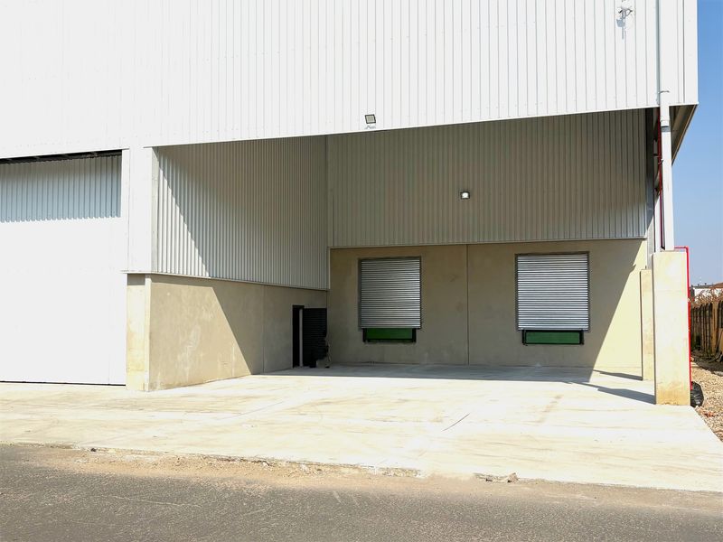 Industrial warehouse exterior featuring a large concrete loading apron, corrugated metal cladding, and secure roller shutter access points.