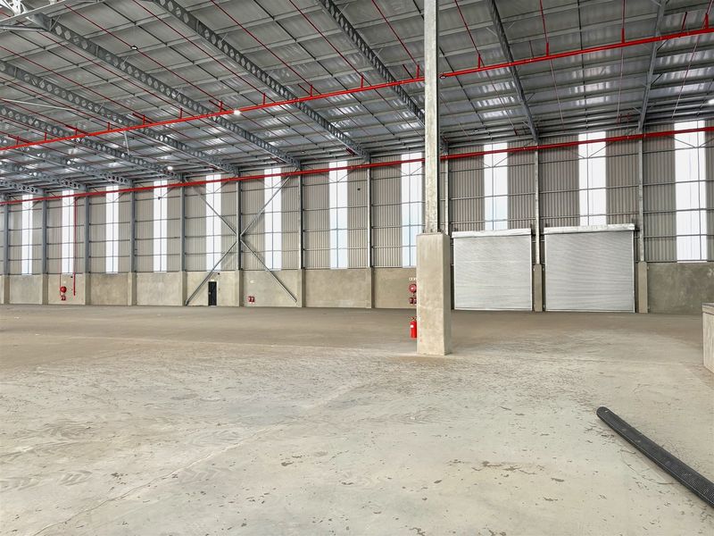 Spacious industrial warehouse featuring a high-clearance steel portal frame, concrete flooring, integrated fire sprinkler system, and multiple roller shutter doors for efficient access.