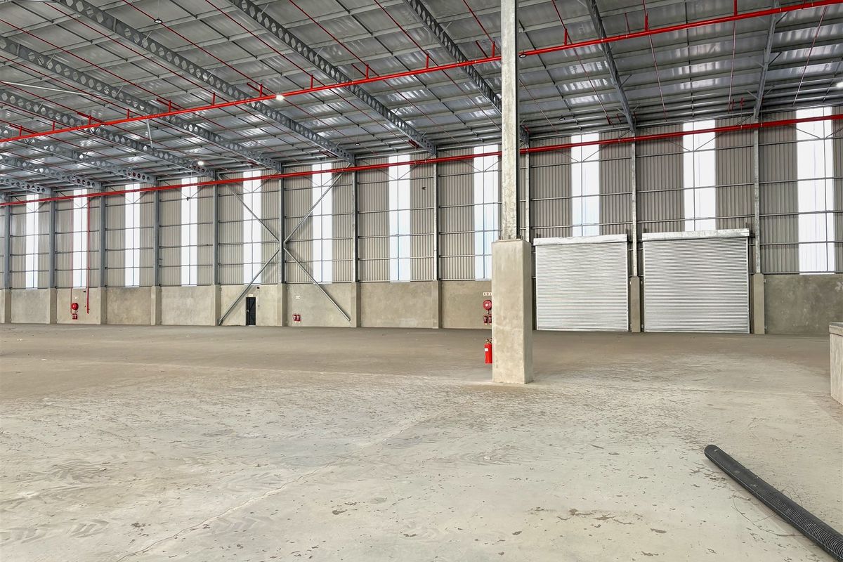 Spacious industrial warehouse featuring a high-clearance steel portal frame, concrete flooring, integrated fire sprinkler system, and multiple roller shutter doors for efficient access.