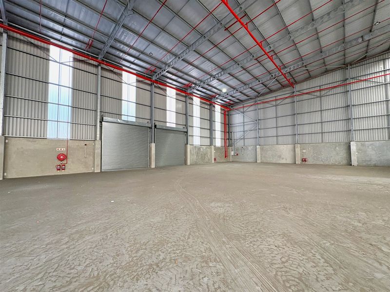 Spacious industrial warehouse unit featuring high ceilings, concrete flooring, roller shutter doors, and an integrated fire sprinkler system.