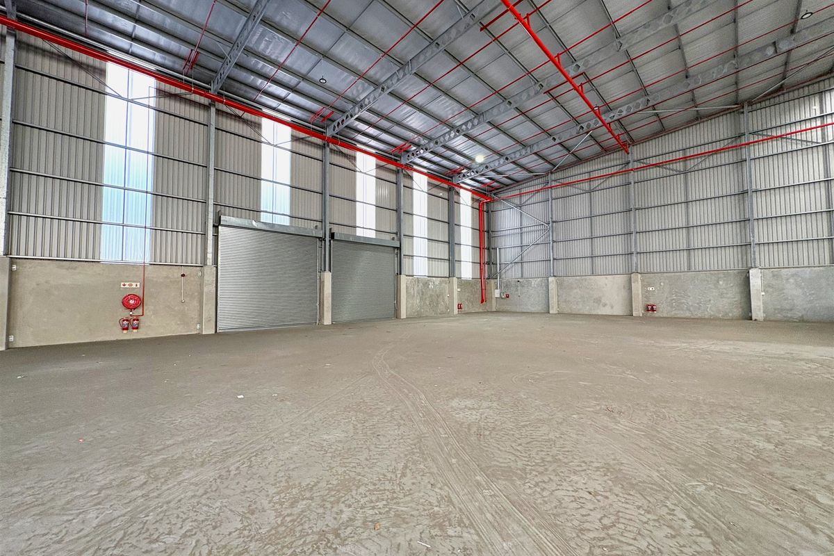 Spacious industrial warehouse unit featuring high ceilings, concrete flooring, roller shutter doors, and an integrated fire sprinkler system.
