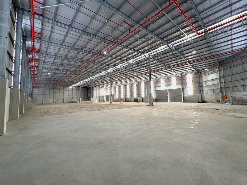 Spacious industrial warehouse featuring high ceilings with exposed steel trusses, fire sprinkler system, polished concrete flooring, and ample natural light through wall panels.