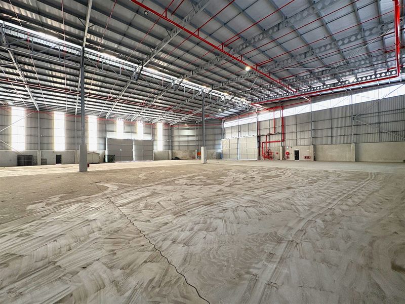 Spacious industrial warehouse featuring high ceilings with exposed steel trusses, fire sprinkler system, concrete flooring, and large sliding access doors.