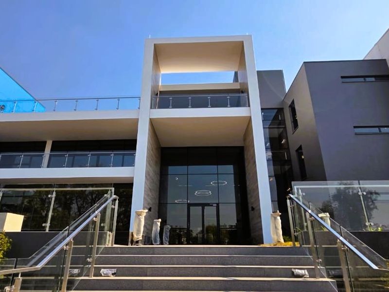 Modern office building facade featuring extensive glass curtain walls, stone cladding, and elevated balconies with stainless steel and glass balustrades.