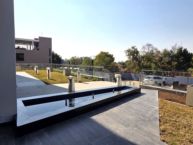 A modern outdoor patio area featuring a sleek water feature, glass balustrades, and tiled flooring, overlooking the surrounding landscape.