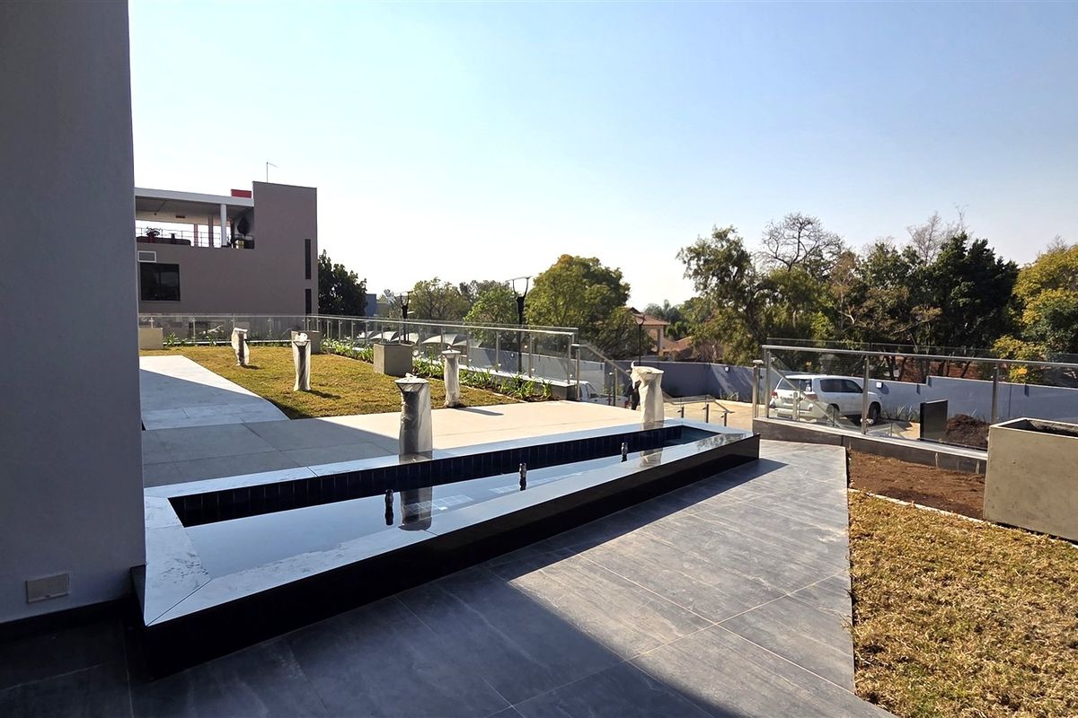A modern outdoor patio area featuring a sleek water feature, glass balustrades, and tiled flooring, overlooking the surrounding landscape.