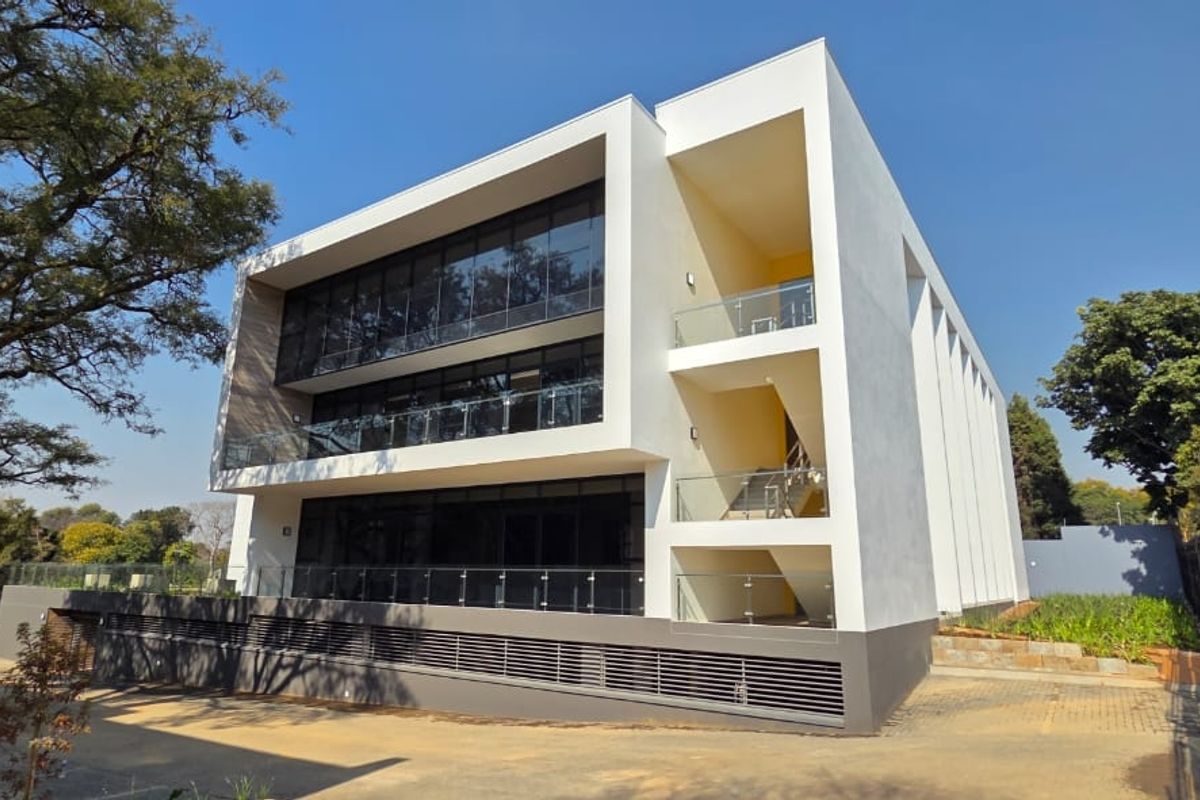 Modern multi-story office building featuring extensive glass curtain walls, external staircases with glass balustrades, and a paved exterior area.