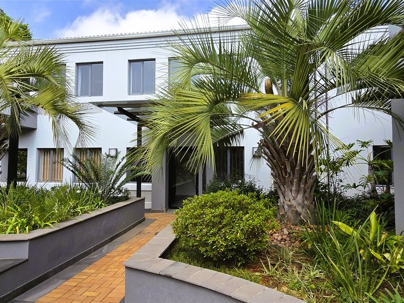 A well-maintained office building exterior featuring a paved walkway, landscaped raised garden beds, and a modern entrance canopy.