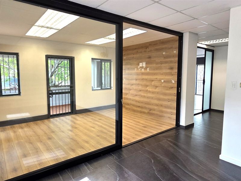 Modern office space featuring glass partitions, wood-look laminate flooring, and a suspended ceiling with recessed lighting, offering a clean and professional work environment.