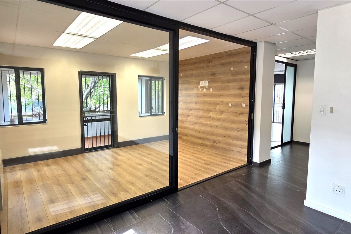 Modern office space featuring glass partitions, wood-look laminate flooring, and a suspended ceiling with recessed lighting, offering a clean and professional work environment.