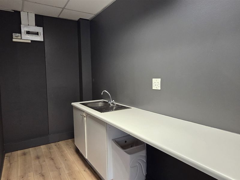 A compact office kitchenette featuring a sink, built-in cabinetry, and a clean countertop, finished with modern dark wall paint and laminate flooring.