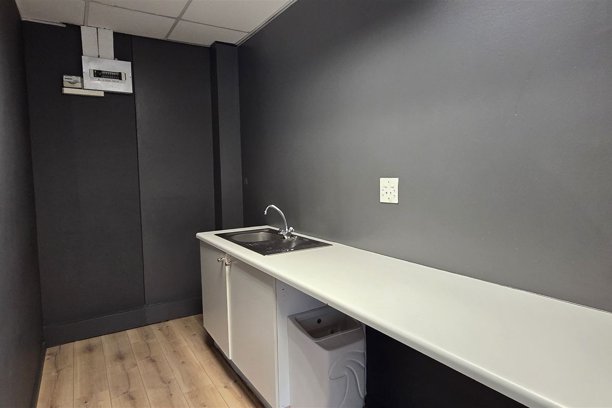 A compact office kitchenette featuring a sink, built-in cabinetry, and a clean countertop, finished with modern dark wall paint and laminate flooring.