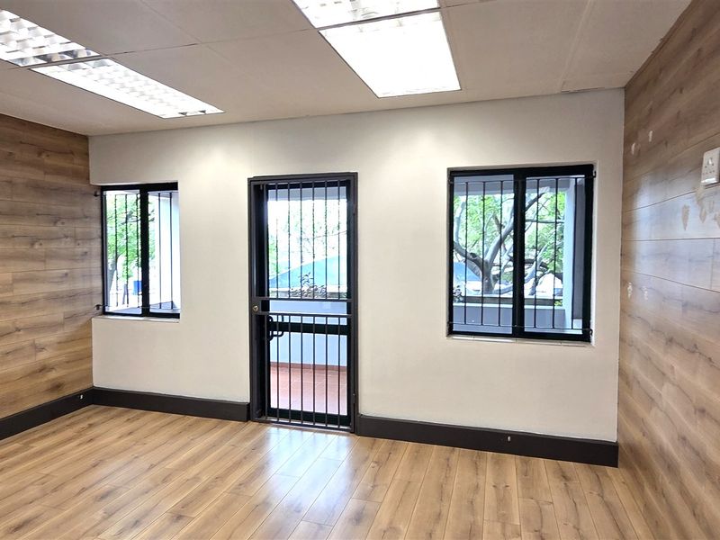 A vacant office space featuring wood-look laminate flooring, matching wall paneling, recessed lighting, and security fixtures on the windows and door.