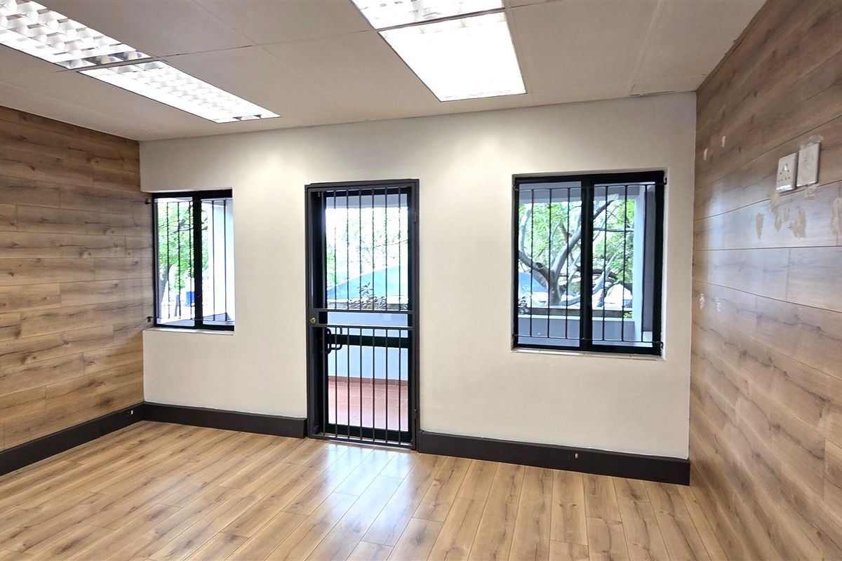 A vacant office space featuring wood-look laminate flooring, matching wall paneling, recessed lighting, and security fixtures on the windows and door.