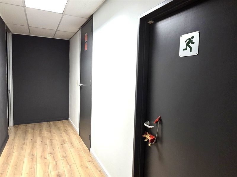 A functional office hallway featuring laminate flooring, a suspended ceiling, and a designated fire exit door.