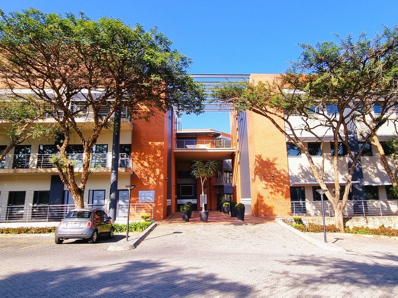 A professional multi-story office building featuring a brick facade, paved driveway, and modern architectural design with integrated balcony railings.