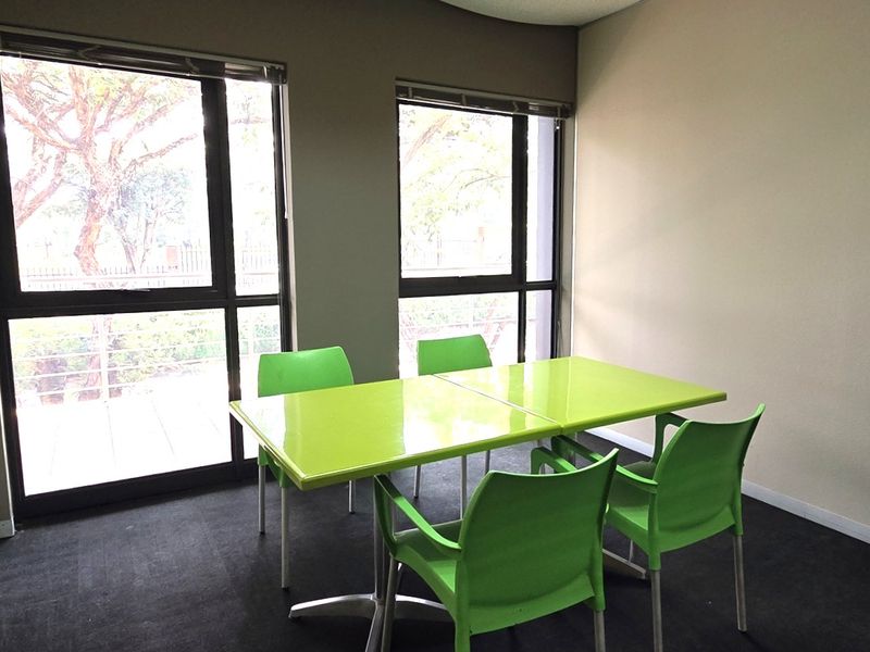 A functional office space featuring large windows for natural light, dark carpeting, and neutral wall finishes.
