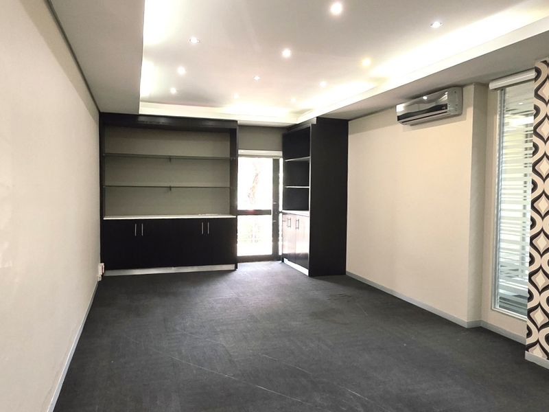 A clean, empty office space featuring built-in storage cabinetry, recessed ceiling lighting, a wall-mounted air conditioning unit, and modern glass partitions.