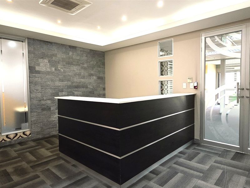 Modern office reception area featuring a built-in desk, stone accent wall, recessed lighting, and glass entry doors with professional finishes.
