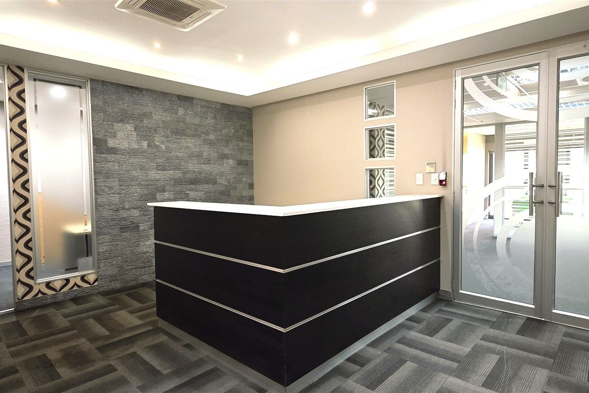 Modern office reception area featuring a built-in desk, stone accent wall, recessed lighting, and glass entry doors with professional finishes.