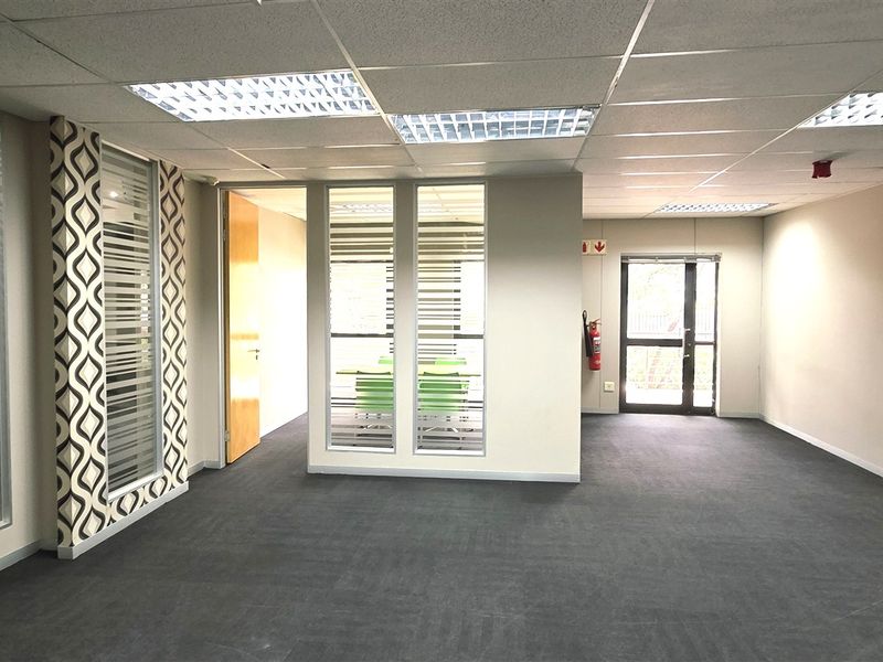 Spacious open-plan office area featuring glass partitions, suspended ceilings with recessed lighting, and neutral carpeting, providing a professional and versatile workspace.