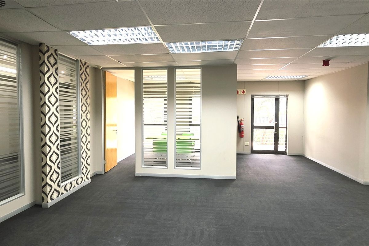 Spacious open-plan office area featuring glass partitions, suspended ceilings with recessed lighting, and neutral carpeting, providing a professional and versatile workspace.