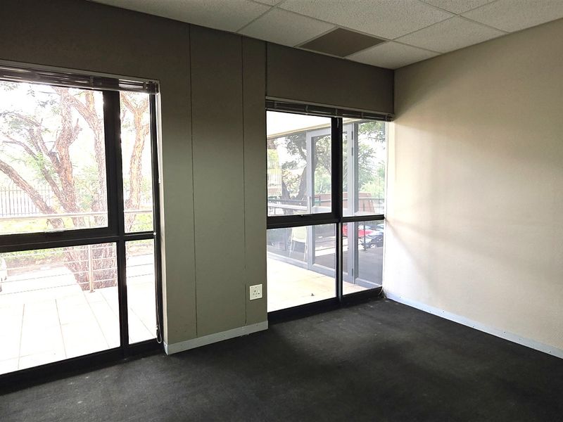 A vacant office space featuring large aluminium-framed windows, carpeted flooring, and integrated electrical and data connectivity points.
