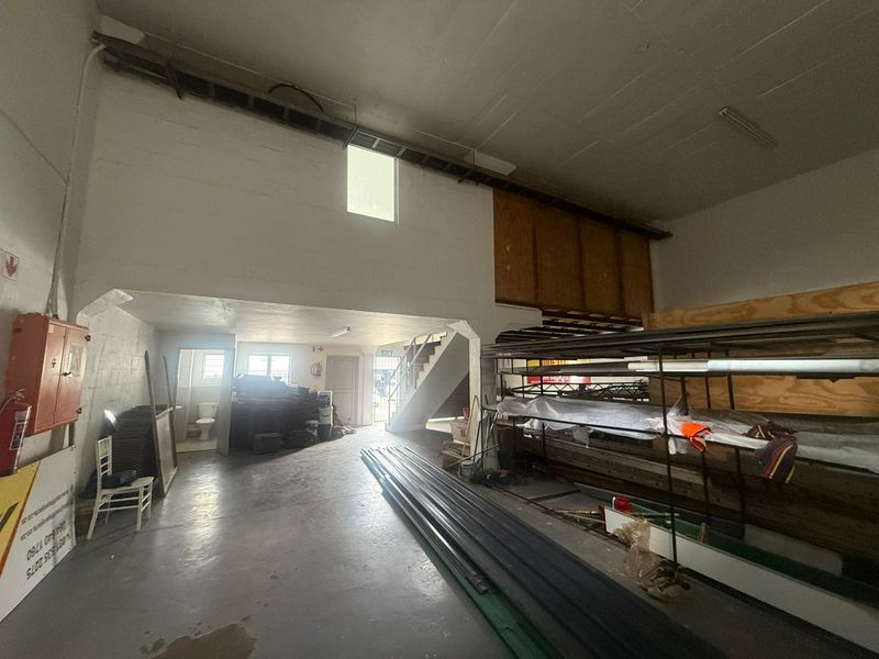 Spacious industrial utility area featuring concrete flooring, a mezzanine level, staircase, and integrated fire safety equipment, suitable for storage or workshop use.