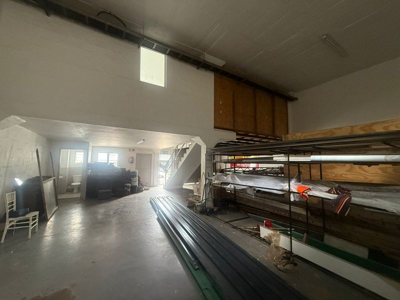 Industrial utility space featuring concrete flooring, a mezzanine level, staircase, and an integrated bathroom, suitable for storage or workshop use.